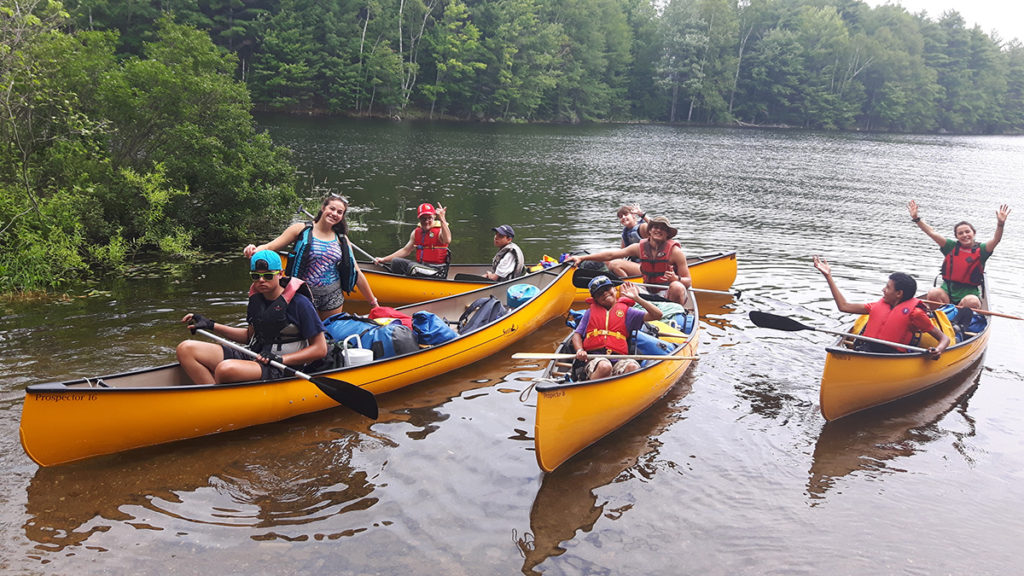 Out-tripping Adventure Camp - A brigade of canoes paddle twards shore