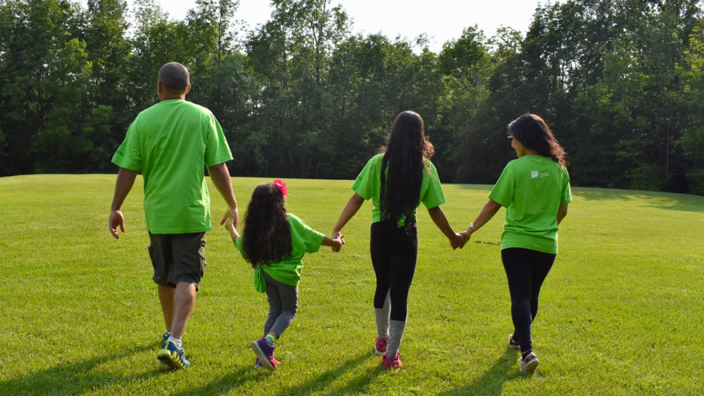 Family Camp - A family walks away in a green field wearing matching t-shirts